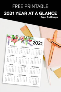 2021 one page calendar with floral elements lying on a stack of notebooks and a pen with text overlay- free printable 2021 year at a glance