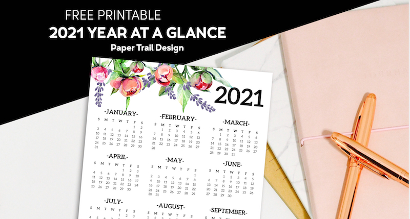 2021 one page calendar with floral elements lying on a stack of notebooks and a pen with text overlay- free printable 2021 year at a glance